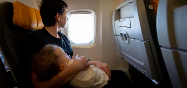 Mutter mit Kleinkind auf dem Schoß blickt am Fensterplatz aus dem Flugzeugfenster